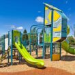 Colorful outdoor playground with a bright green slide and blue climbing frames under a clear blue sky.