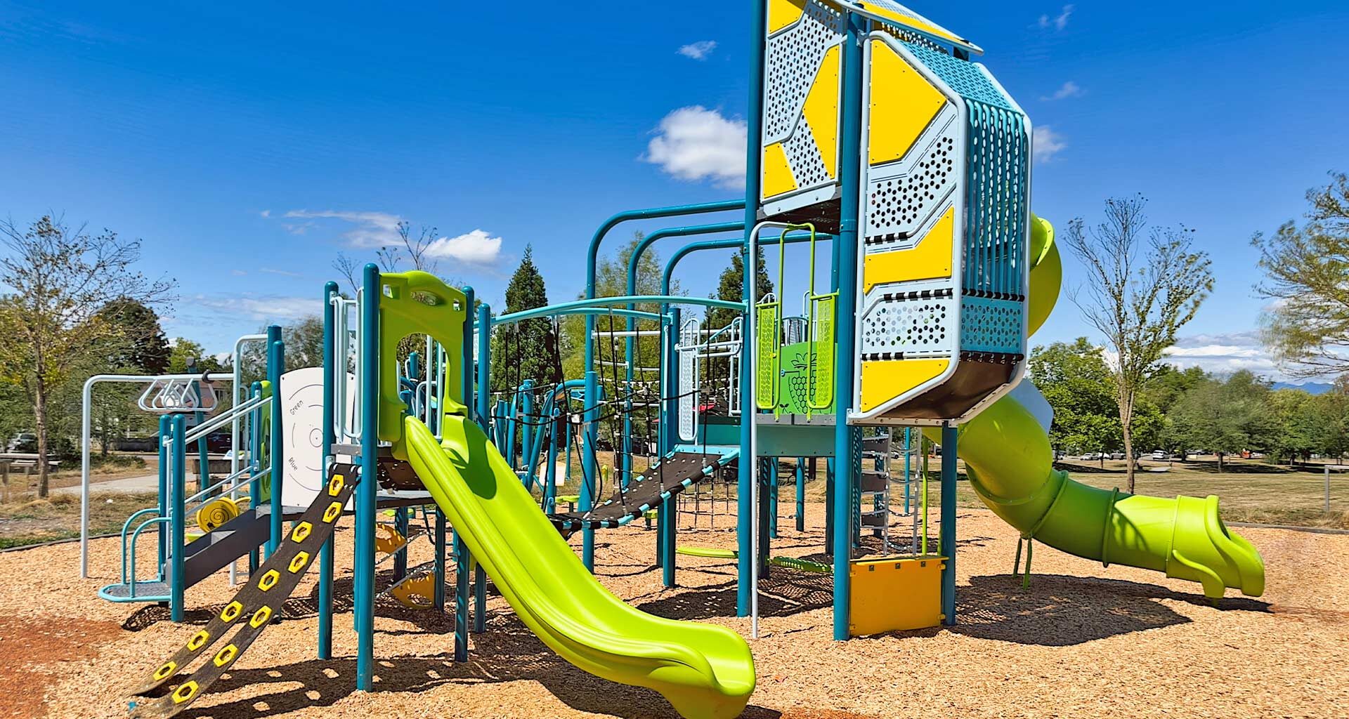 Colorful outdoor playground with a bright green slide and blue climbing frames under a clear blue sky.